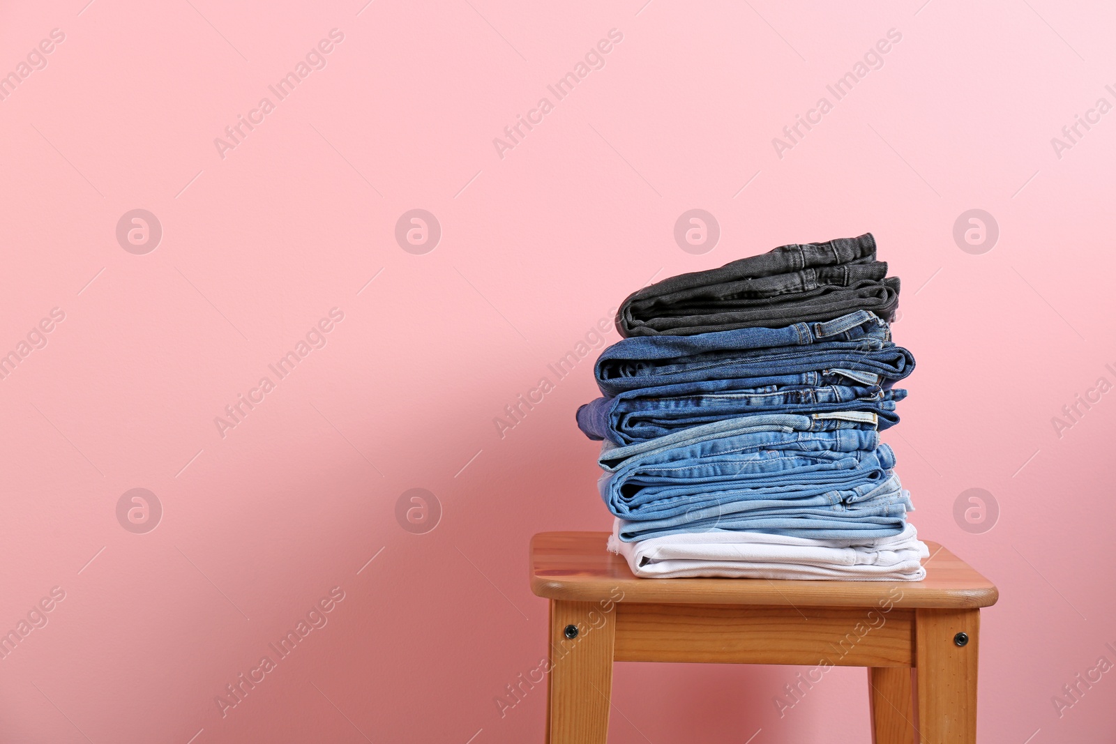 Photo of Stack of different jeans on stool against color background