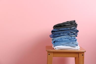 Photo of Stack of different jeans on stool against color background