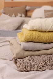 Stack of different folded blankets and clothes on bed, closeup. Home textile