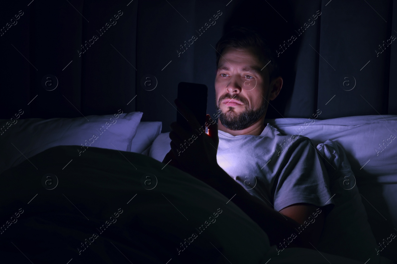 Photo of Man using smartphone in bed at night. Internet addiction