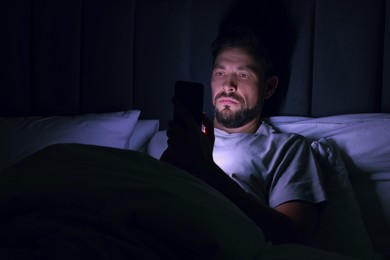 Photo of Man using smartphone in bed at night. Internet addiction