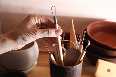 Photo of Woman taking clay crafting tool from cup in workshop, closeup