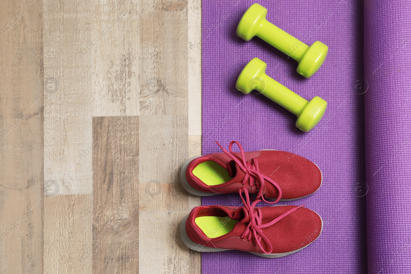 Photo of Dumbbells, sneakers and mat on wooden floor, above view. Space for text