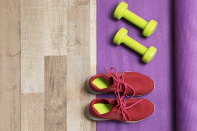 Photo of Dumbbells, sneakers and mat on wooden floor, above view. Space for text