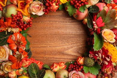 Beautiful autumnal wreath with flowers, berries and fruits on wooden background, closeup. Space for text