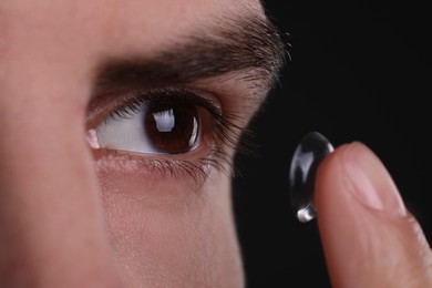 Photo of Closeup view of man putting contact lens in his eye against black background