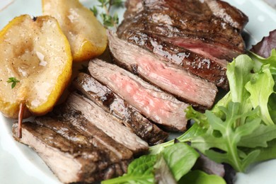 Photo of Pieces of delicious roasted beef meat, caramelized pear and greens on plate, closeup
