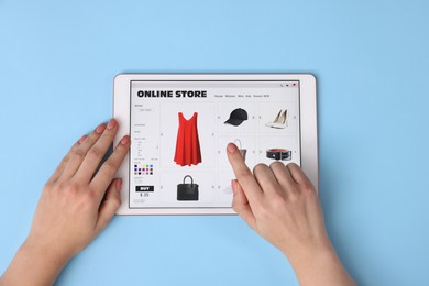 Woman with tablet shopping online on light blue background, top view