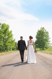 Photo of Bride and groom walking away on highway