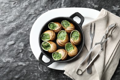 Photo of Delicious cooked snails in baking dish served on grey textured table, flat lay