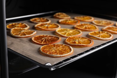 Photo of Many dry orange slices on parchment paper in oven