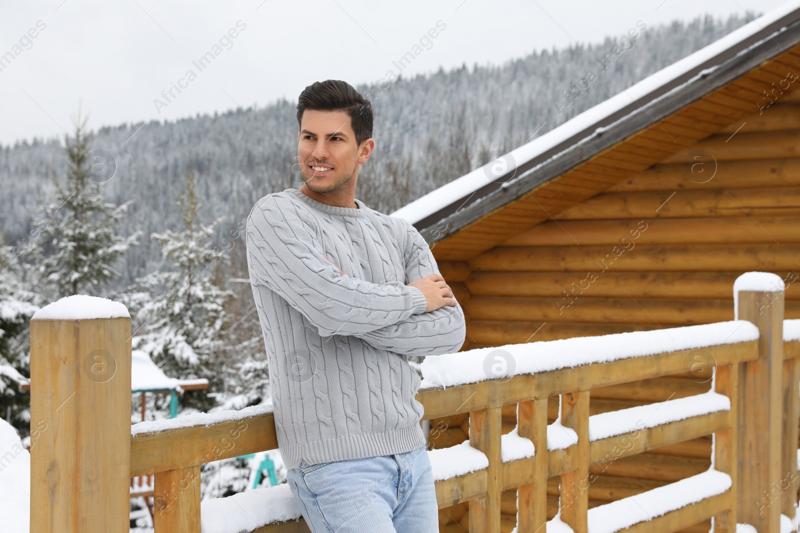 Photo of Happy man in warm sweater near wooden railing outdoors