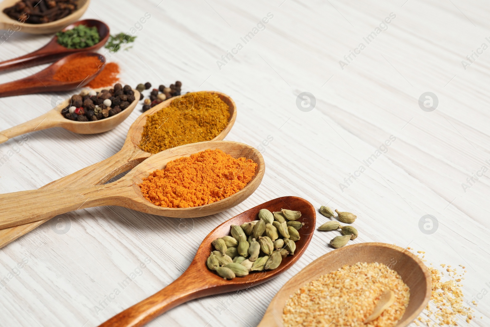 Photo of Spoons with different spices on white wooden table, closeup. Space for text