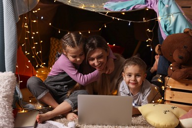 Photo of Mother and her children with laptop in play tent at home