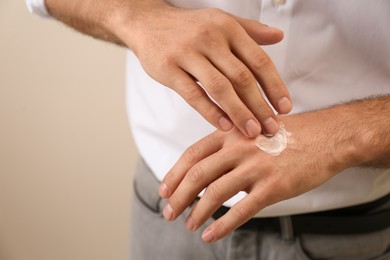 Photo of Man applying cream onto hand on beige background, closeup