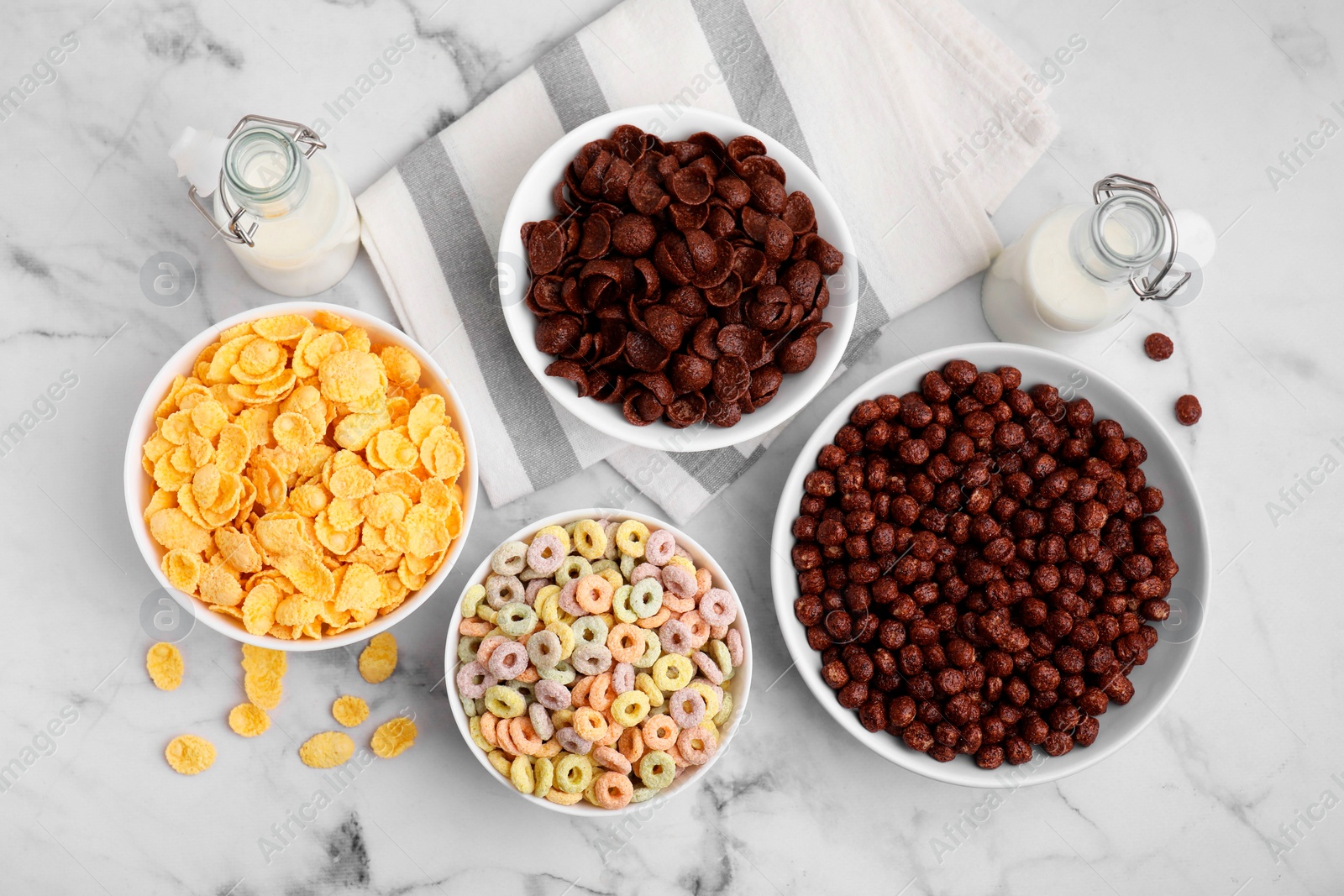 Photo of Different delicious breakfast cereals and milk on white marble table, flat lay