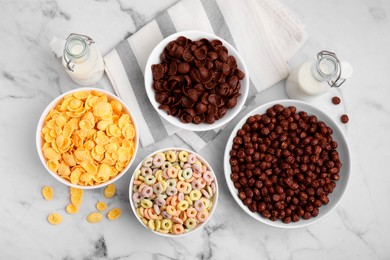 Different delicious breakfast cereals and milk on white marble table, flat lay