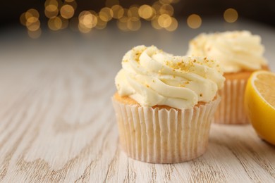 Photo of Tasty cupcakes with cream and lemon zest on white wooden table, closeup. Space for text