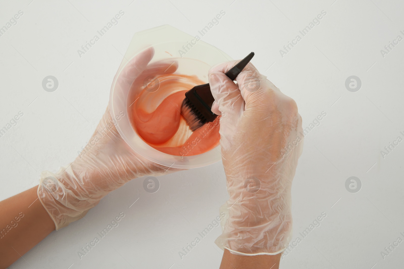 Photo of Woman preparing hair dye in bowl at white table, closeup