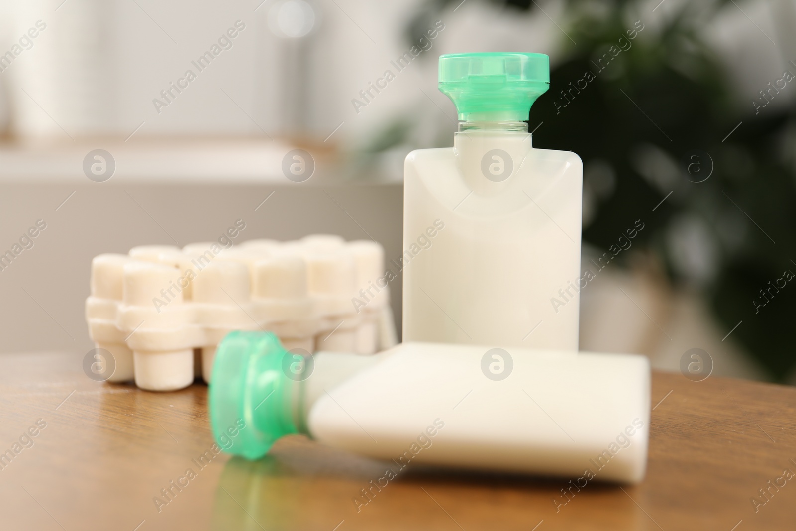 Photo of Mini bottles of cosmetic products and soap on wooden table against blurred background, closeup