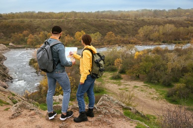 Couple of travelers with backpacks and map planning trip in mountains, back view. Autumn vacation