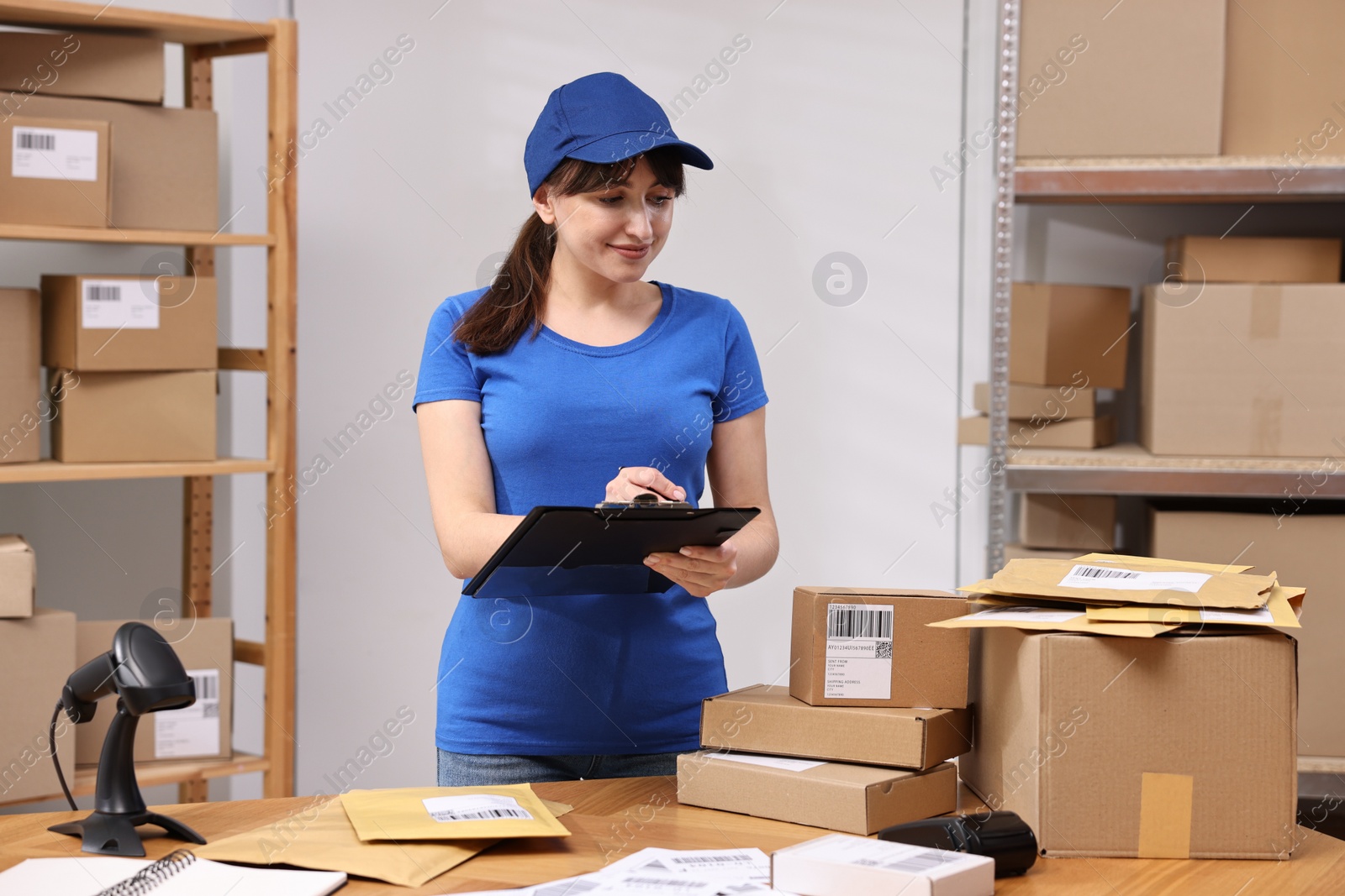 Photo of Parcel packing. Post office worker with clipboard at wooden table indoors