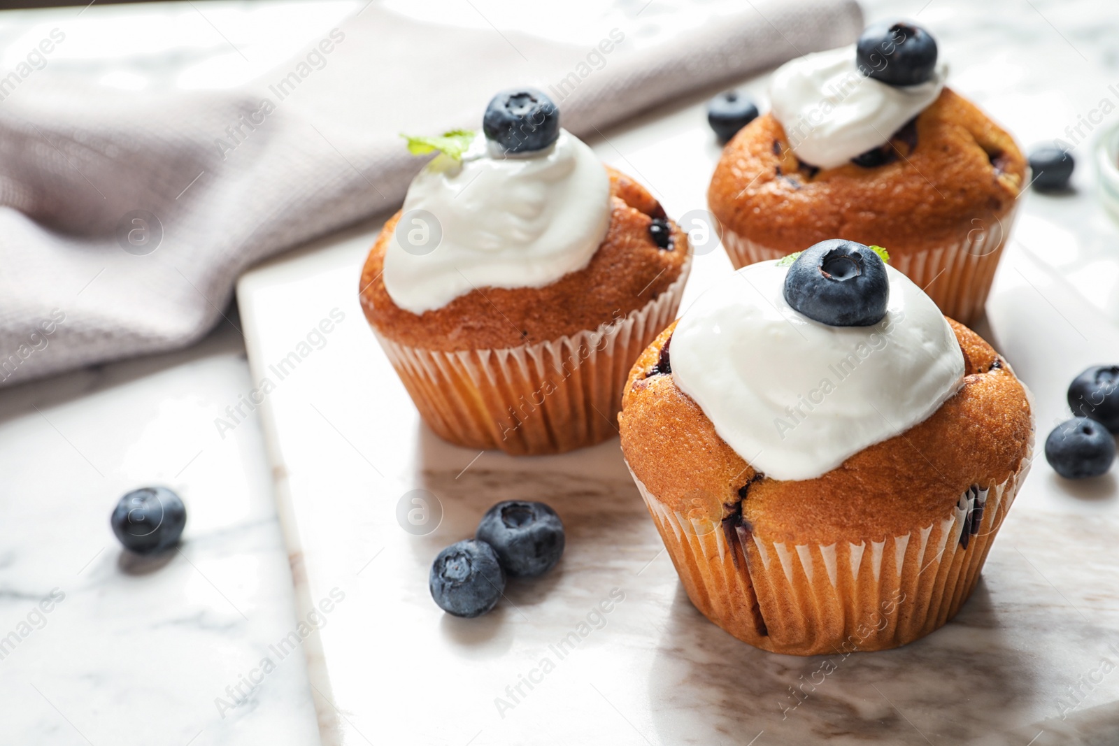 Photo of Marble board with tasty muffins, cream and blueberries on table