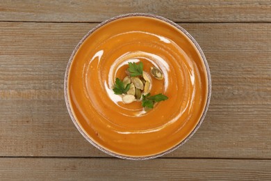 Photo of Delicious pumpkin soup with seeds and parsley in bowl on wooden table, top view
