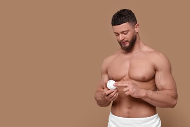 Photo of Handsome man applying body cream on pale brown background, space for text