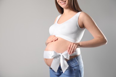Photo of Young pregnant woman with bow on her belly against grey background, closeup. Time to give birth