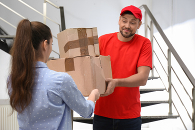 Photo of Emotional courier giving damaged cardboard boxes to client indoors. Poor quality delivery service