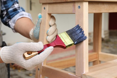 Photo of Man varnishing wooden step stool outdoors, closeup