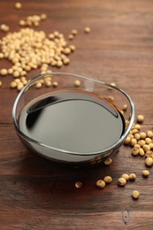 Photo of Soy sauce in bowl and soybeans on wooden table