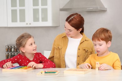 Photo of Happy mother and children playing with different math game kits at white marble table in kitchen. Study mathematics with pleasure