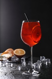 Photo of Glass of tasty Aperol spritz cocktail with orange slices and ice cubes on table against black background