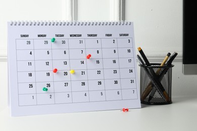 Photo of Timetable. Calendar with drawing pins and stationery on white table indoors