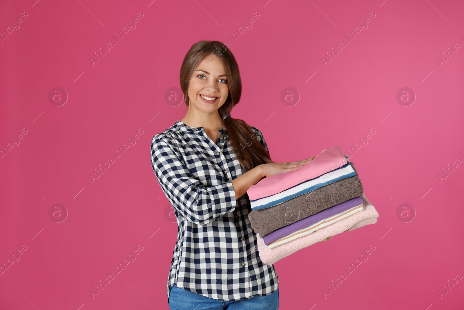 Photo of Happy young woman holding clean laundry on color background