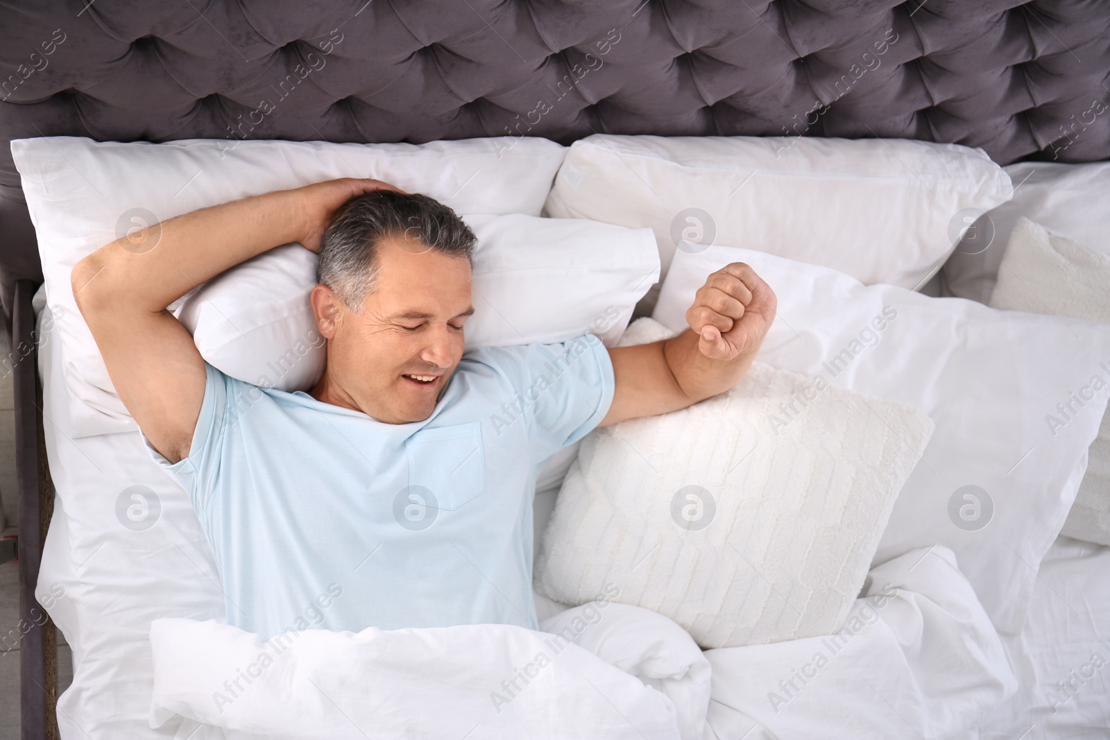 Photo of Man yawning after sleeping on comfortable pillow in bed at home