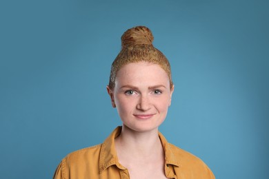 Young woman dyeing her hair with henna on light blue background