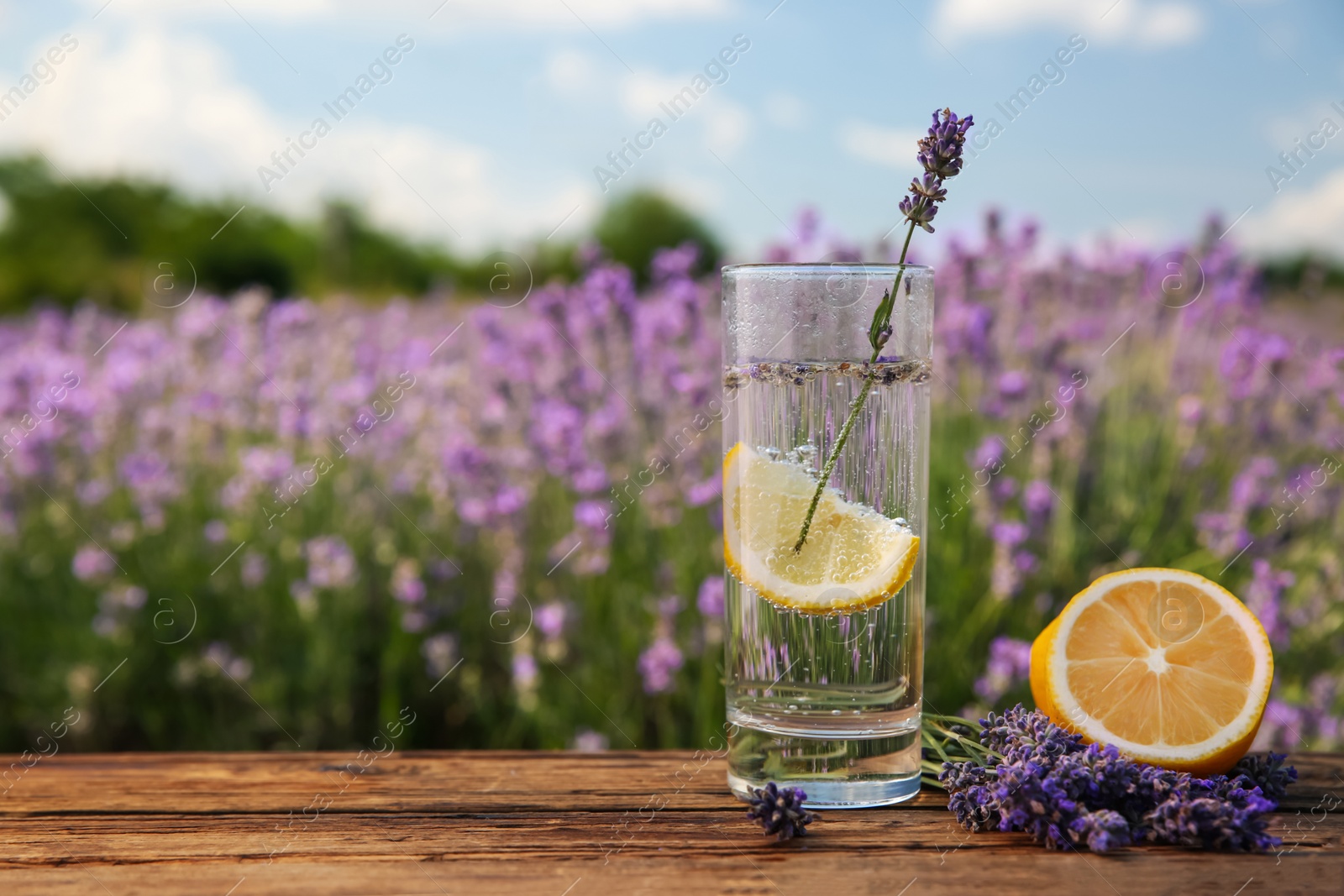 Photo of Lemonade with lemon slice and lavender flowers on wooden table outdoors, closeup. Space for text