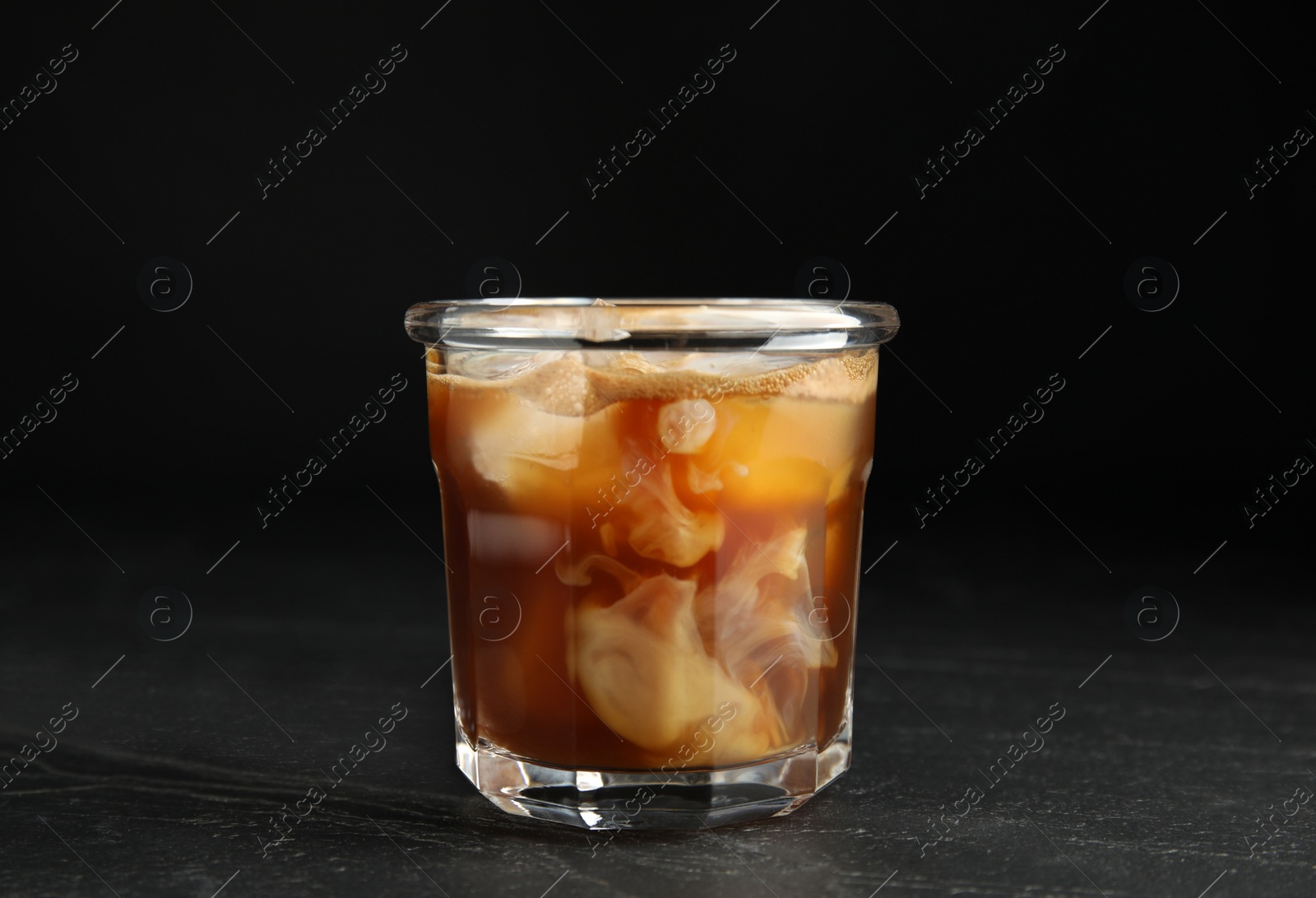 Photo of Glass of coffee with milk and ice cubes on black slate table