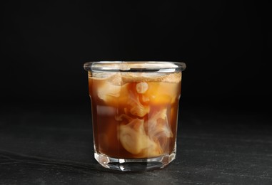 Glass of coffee with milk and ice cubes on black slate table