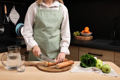 Photo of Woman in clean apron cutting baguette on wooden table at kitchen, closeup