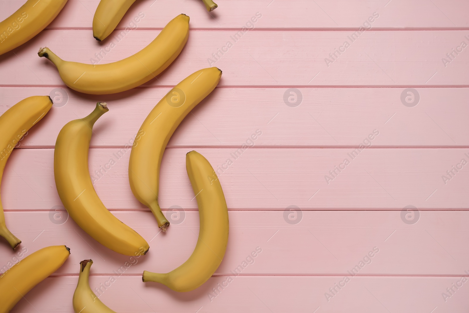 Photo of Ripe yellow bananas on light pink wooden table, flat lay. Space for text