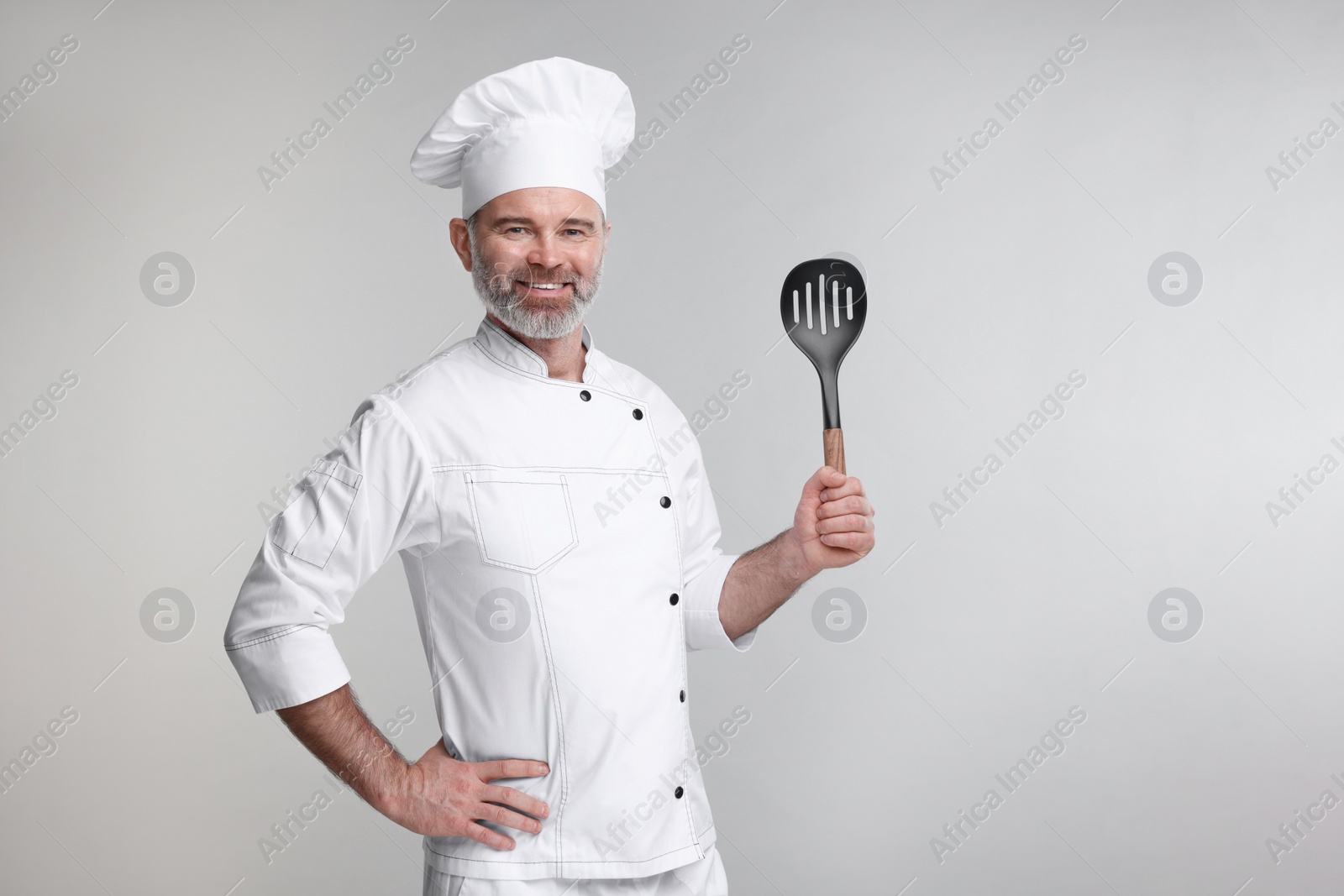 Photo of Happy chef in uniform with spatula on grey background, space for text