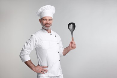 Happy chef in uniform with spatula on grey background, space for text