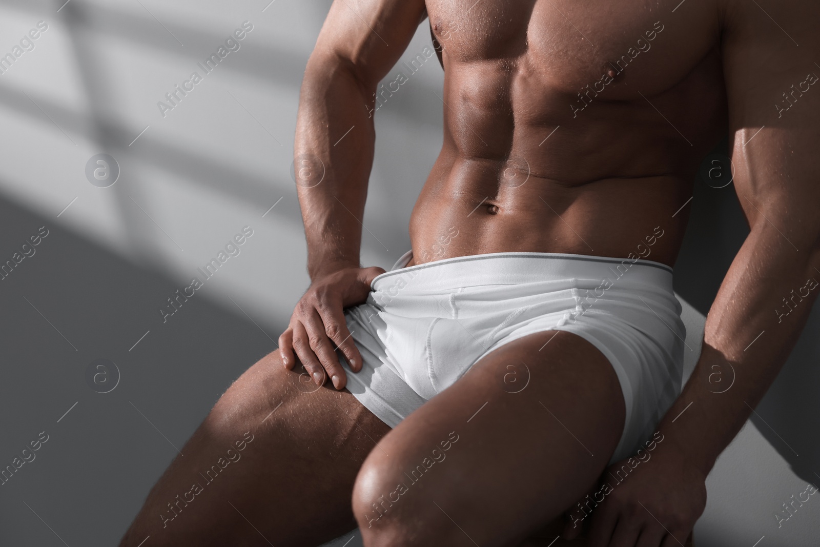 Photo of Young man in stylish white underwear sitting on chair near grey wall, closeup