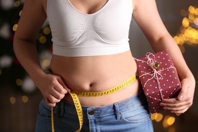 Woman with gift box and measuring tape indoors, closeup. Overweight problem after New Year party