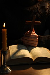 Photo of Woman praying at table with burning candle and Bible, closeup