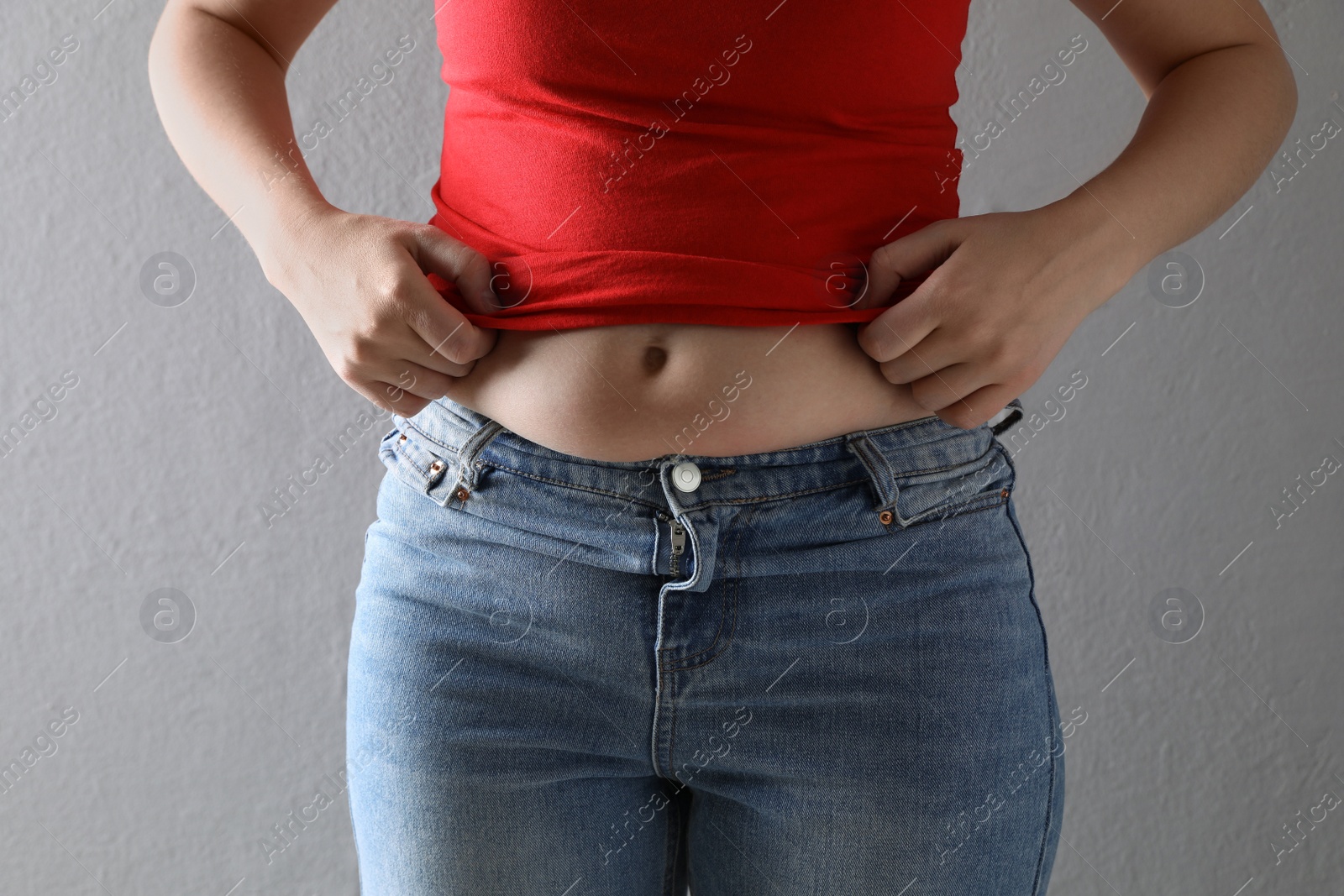 Photo of Woman wearing tight clothes on grey background, closeup. Overweight problem
